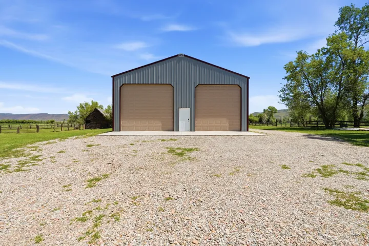 Metal-sided structure featuring two large roll-up doors, a pedestrian entrance, and a gravel foreground