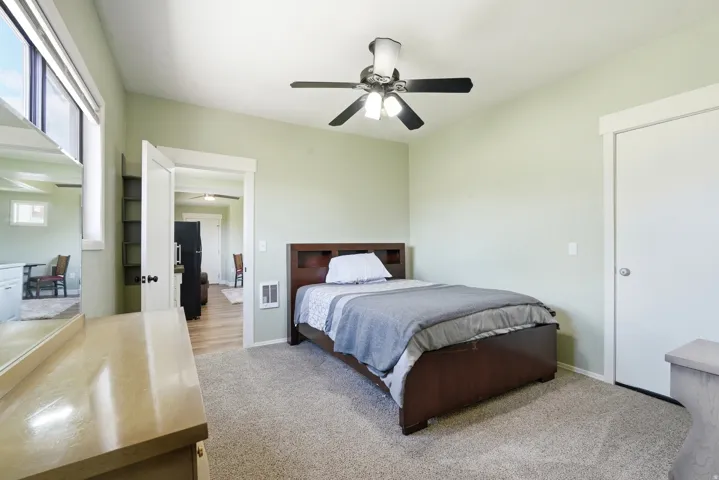 Vaulted ceiling, ceiling fan with integrated lighting, window with white blinds, light-colored carpeting, white trim