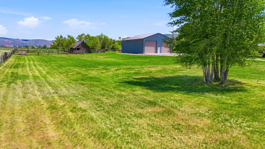 Expansive green space featuring a large outbuilding with multiple garage doors, a rustic wooden structure, and scattered trees
