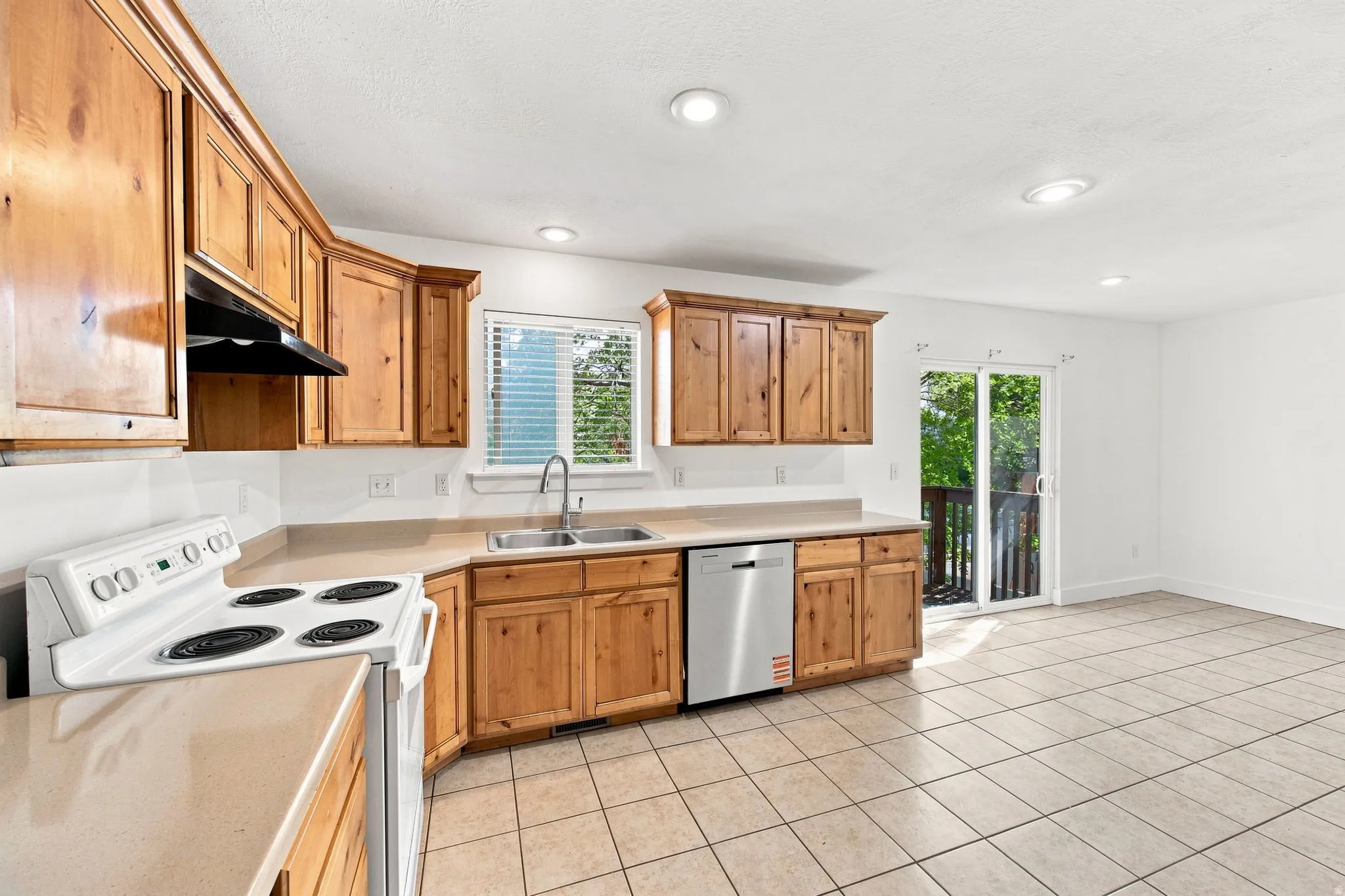 Kitchen featuring wood cabinetry, solid surface countertops, stainless steel dishwasher, tile flooring, and sliding glass door access to an outdoor area