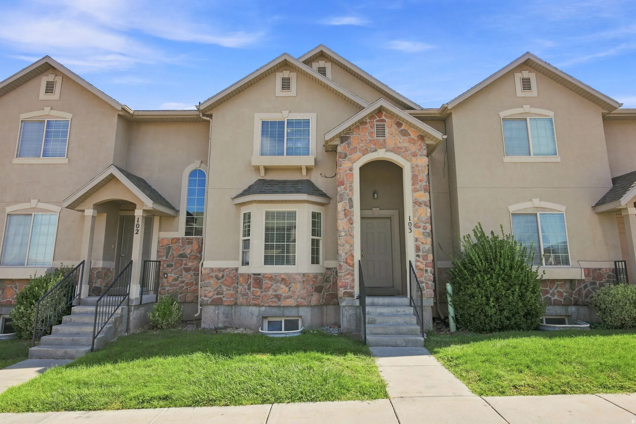 Exterior featuring stucco siding with stone veneer accents, arched entryways, bay windows, and gabled roofs