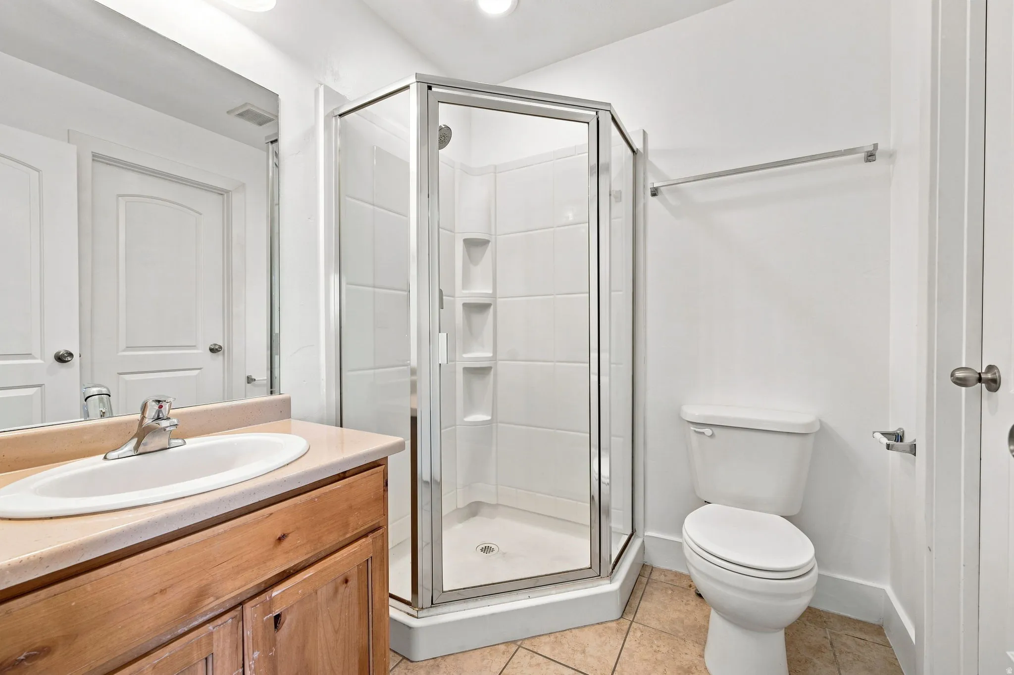 Corner glass-enclosed shower, wood-finish vanity with an integrated sink, polished chrome faucet, and tiled flooring