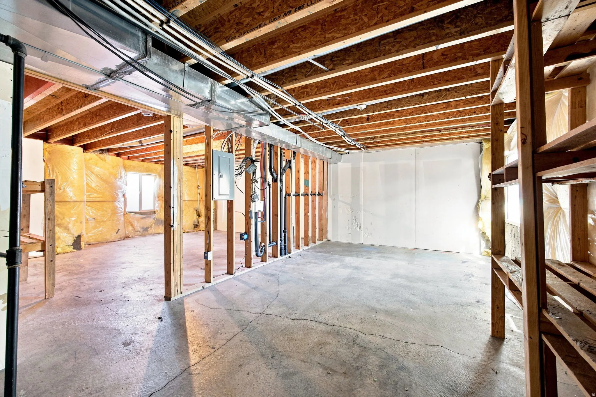 Unfinished basement with exposed ceiling joists, concrete flooring, and visible electrical panel
