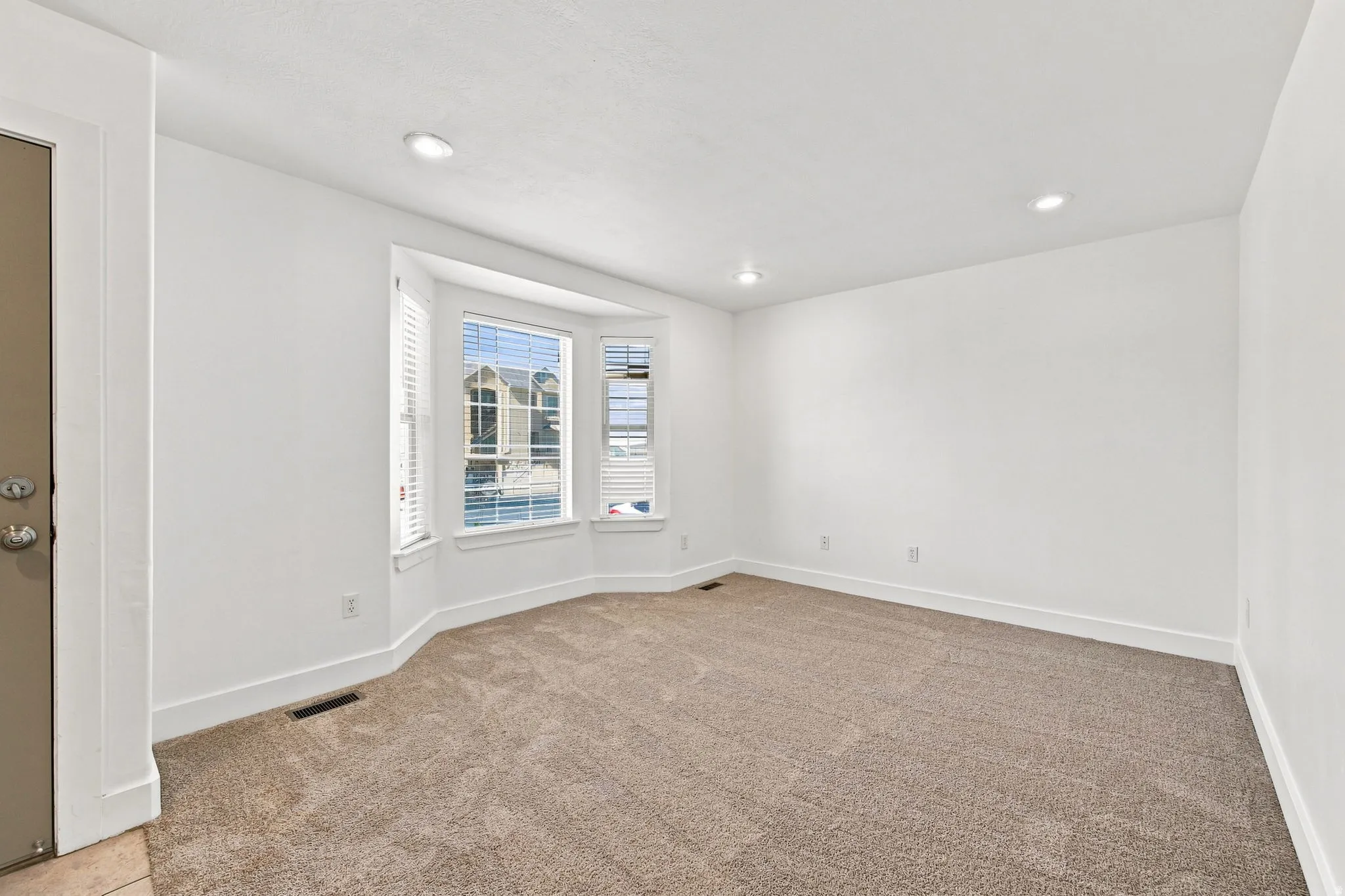 Bay window with white blinds, recessed lighting, and neutral carpet flooring