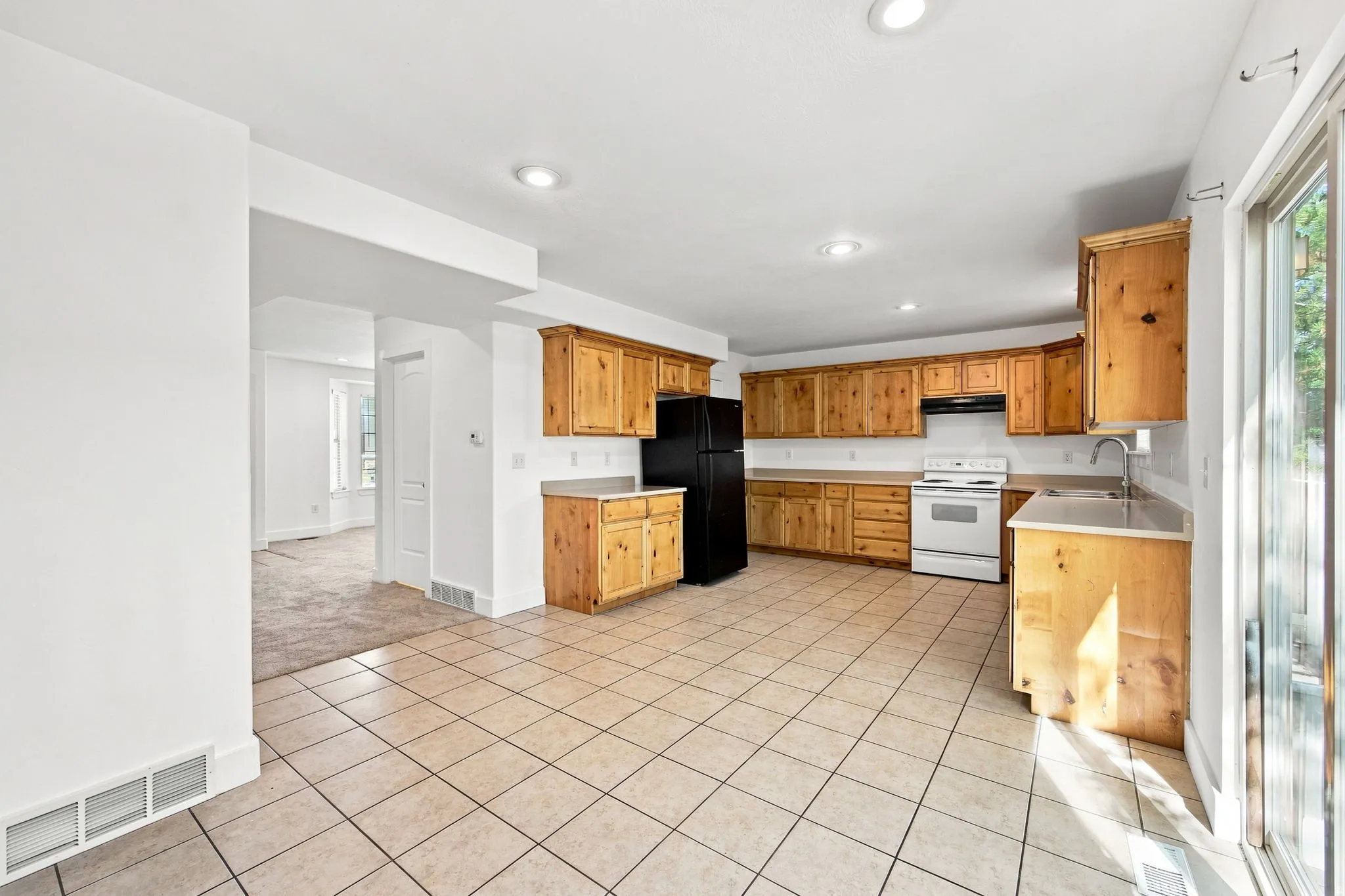 Kitchen featuring abundant light wood cabinetry, a white electric range, a black refrigerator, light-toned countertops, and neutral tile flooring