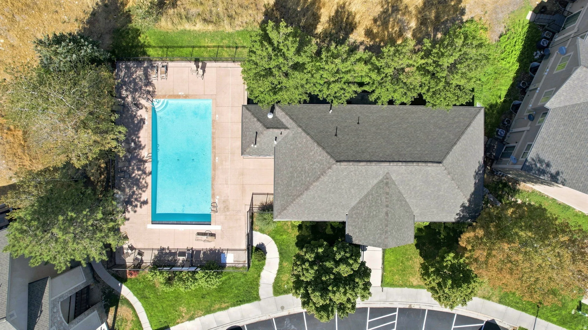 Rectangular swimming pool with surrounding hardscaping, a shingled roof structure, and surrounding trees
