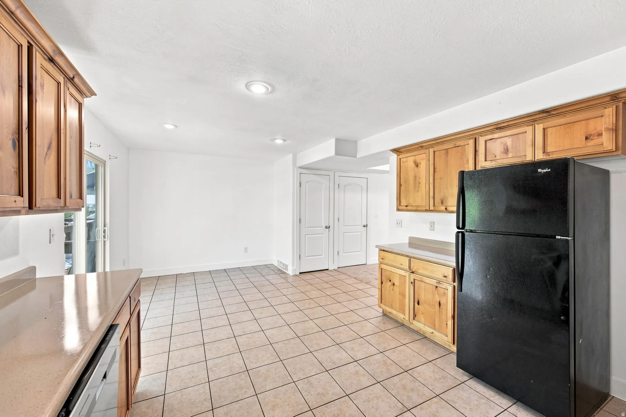Kitchen space featuring light wood cabinetry, neutral countertops, tile flooring, recessed lighting, and a built-in refrigerator