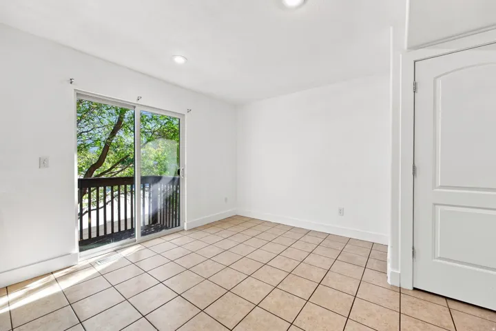 Expansive tile flooring, sliding glass door leading to a balcony with dark wood railing, and recessed lighting