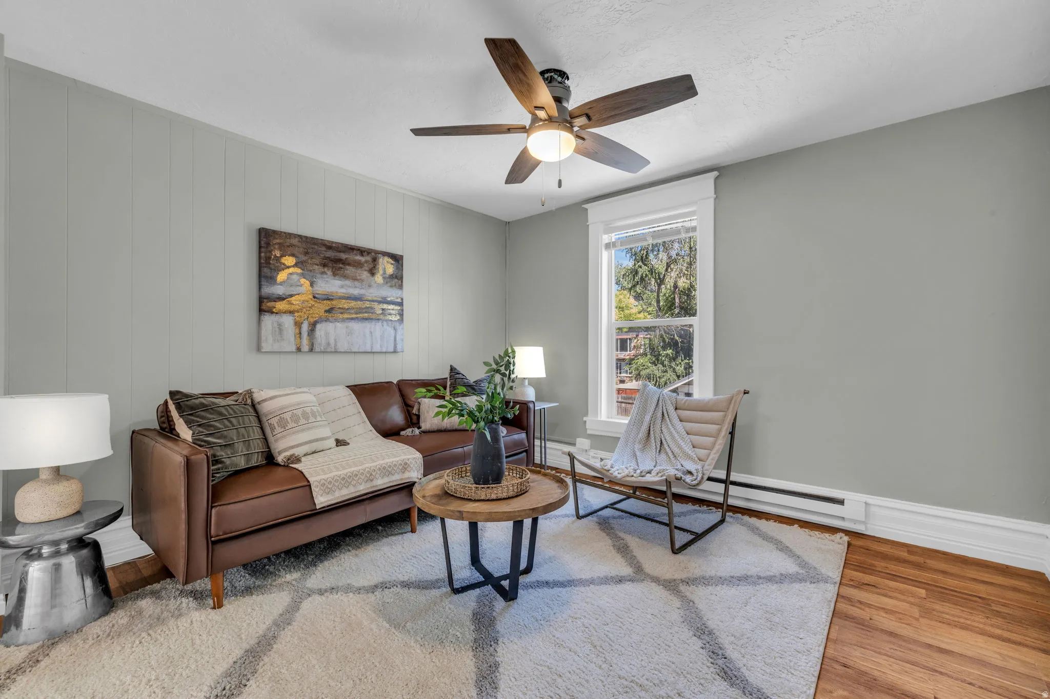 Hardwood flooring, painted paneled accent wall, ceiling fan with integrated lighting, and a window with white trim