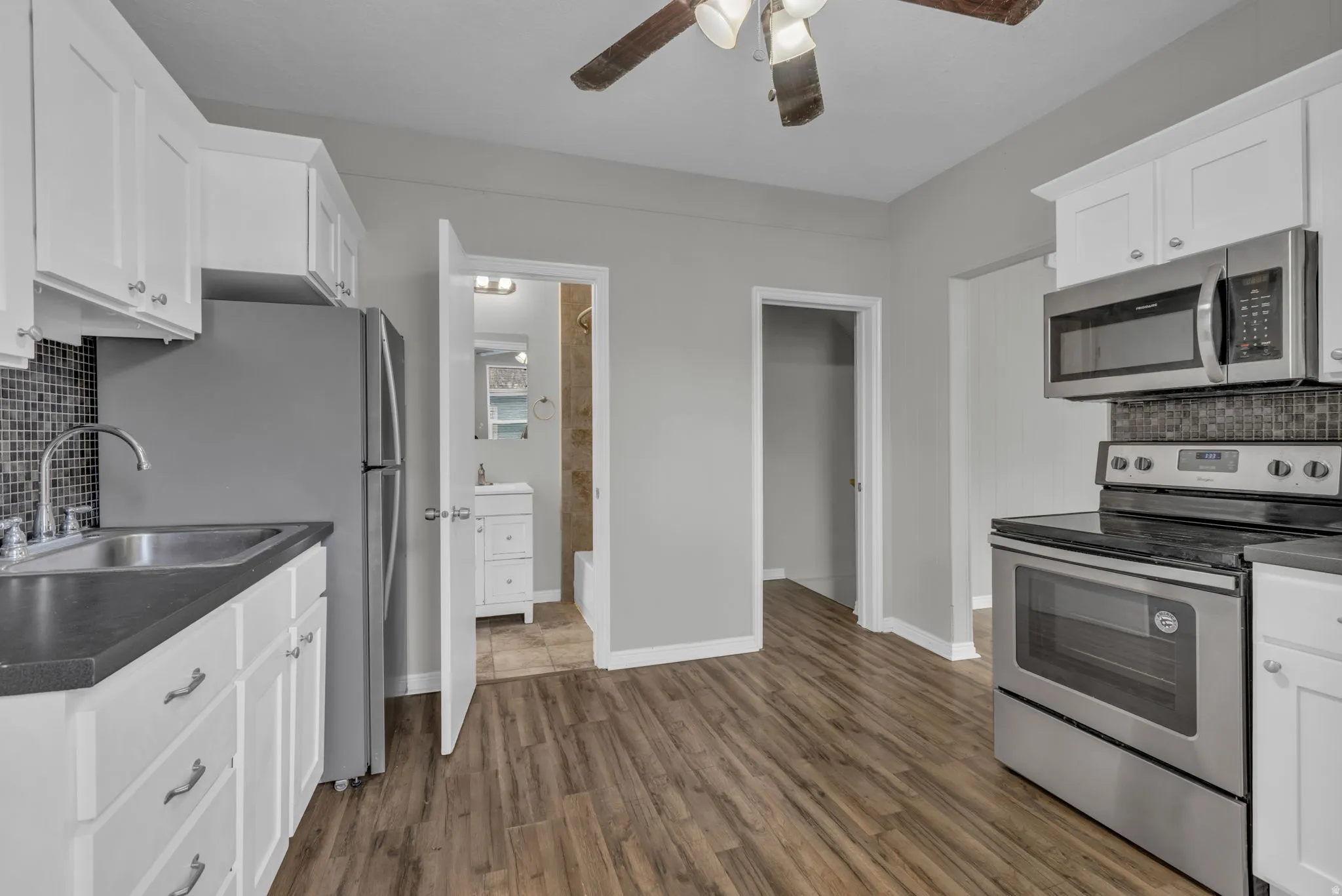 Kitchen featuring wood-finish flooring, white cabinetry with silver hardware, dark countertops, and a mosaic tile backsplash