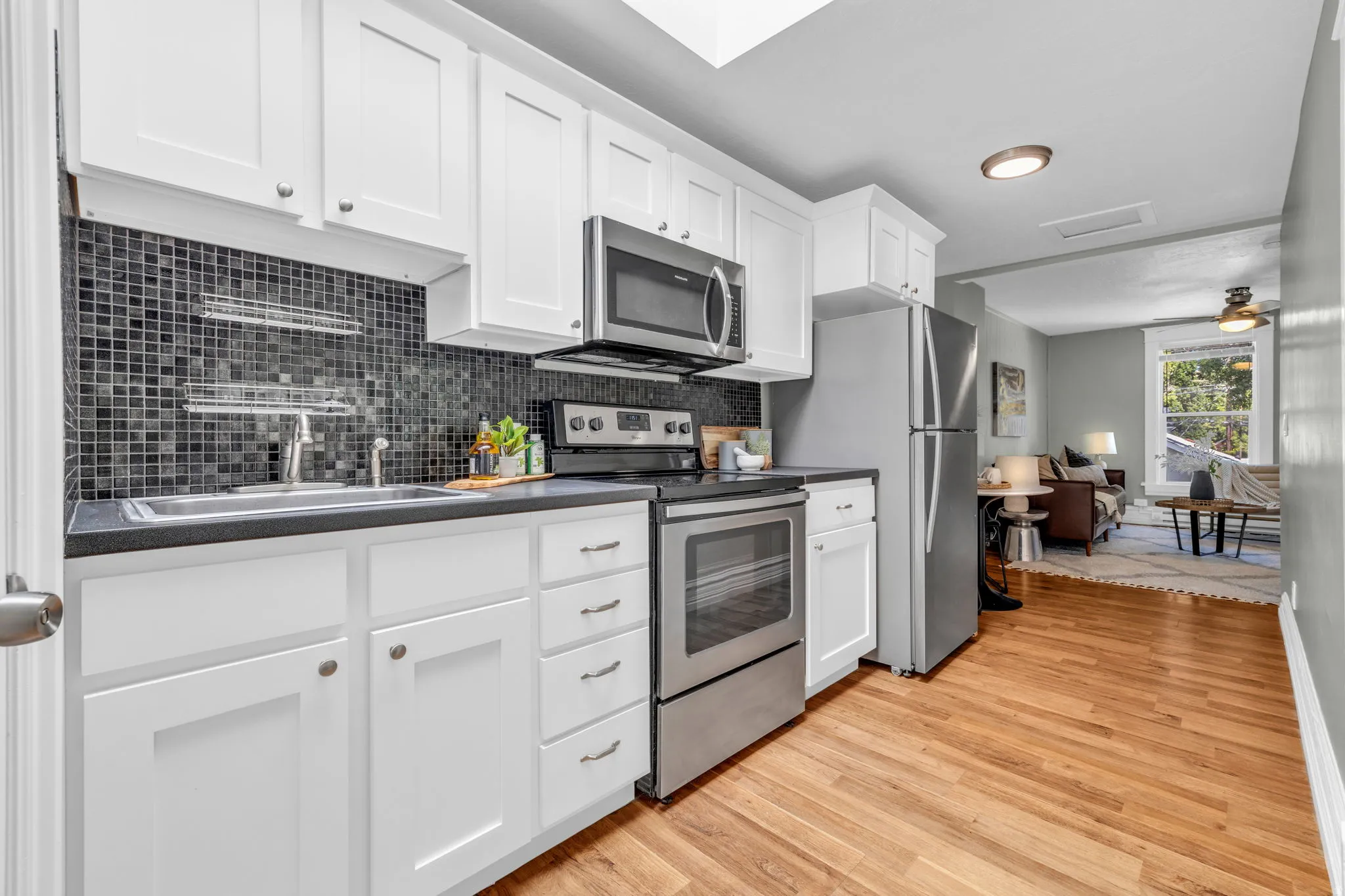 Kitchen featuring white shaker-style cabinetry, stainless steel appliances, dark countertop, mosaic tile backsplash, and wood-finish flooring