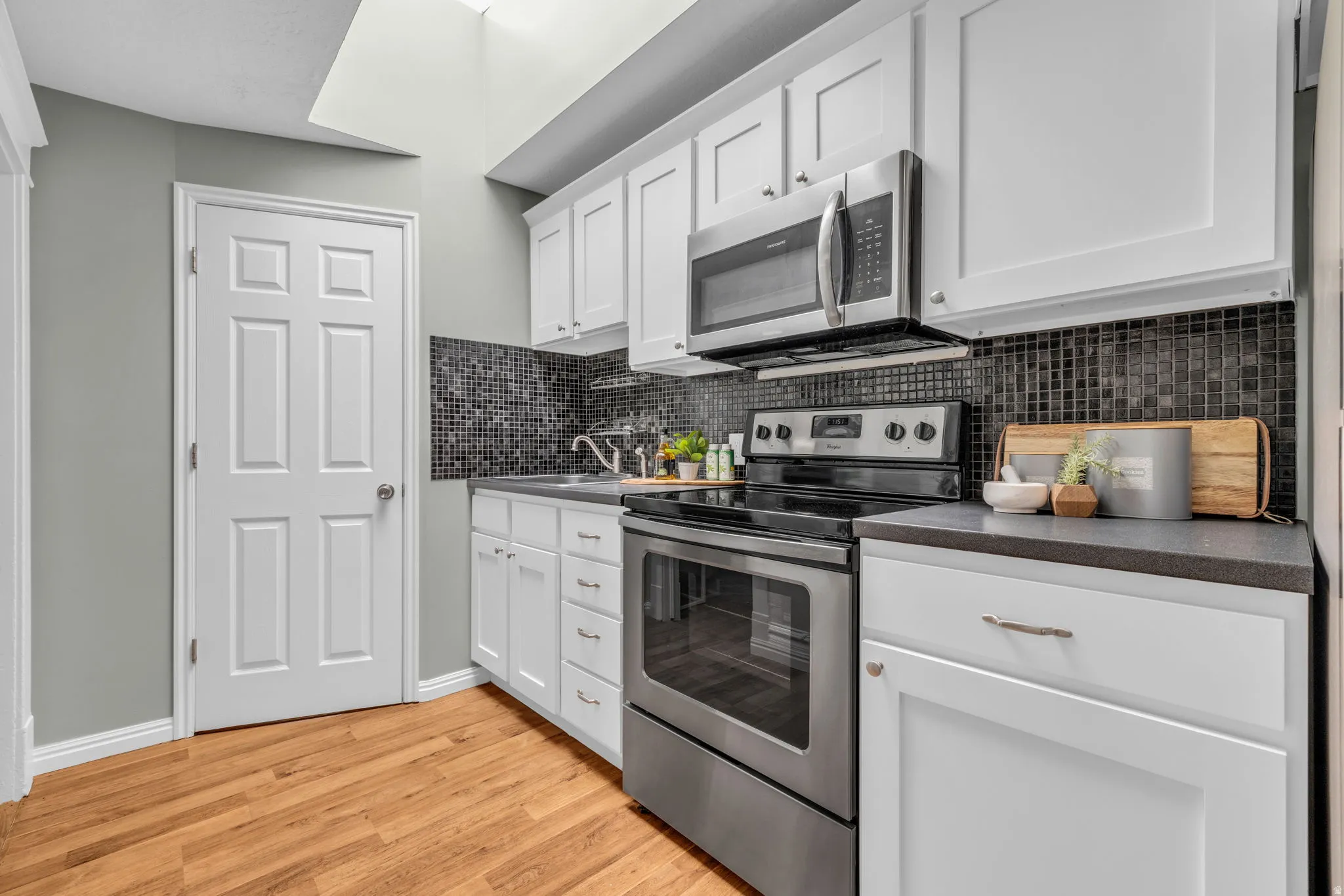 Kitchen featuring white cabinetry, stainless steel appliances, dark mosaic tile backsplash, and wood-finish flooring