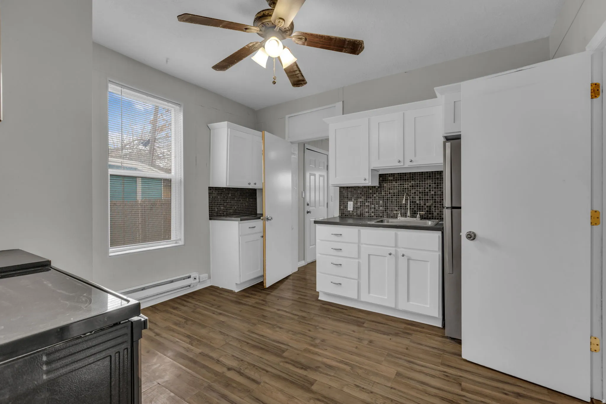 Kitchen featuring wood-finish flooring, white cabinetry, dark countertops, a mosaic tile backsplash, and a stainless steel refrigerator