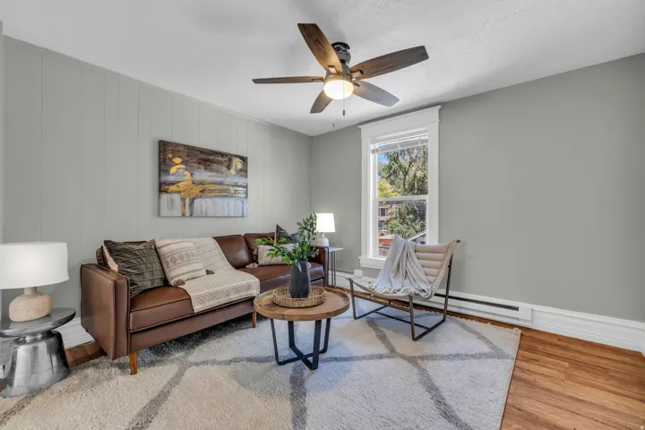 Hardwood flooring, painted paneled accent wall, ceiling fan with integrated lighting, and a window with white trim