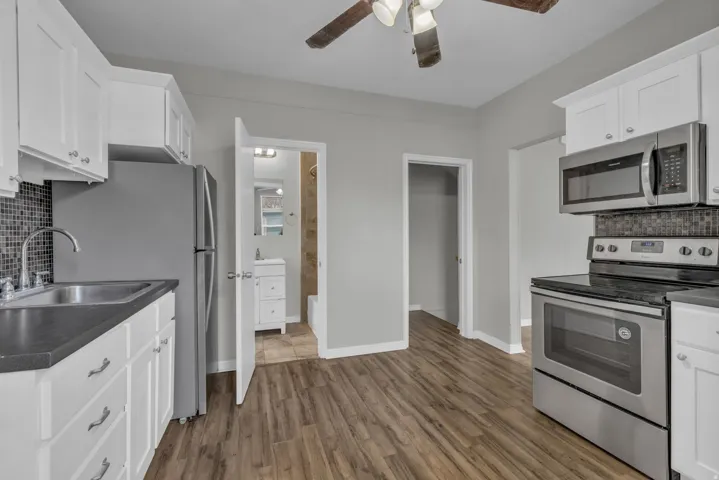 Kitchen featuring wood-finish flooring, white cabinetry with silver hardware, dark countertops, and a mosaic tile backsplash