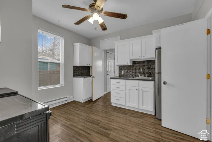 Kitchen featuring wood-finish flooring, white cabinetry, dark countertops, a mosaic tile backsplash, and a stainless steel refrigerator