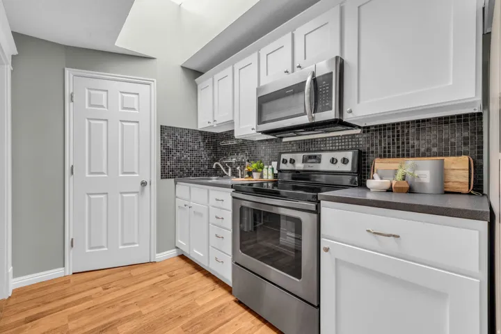Kitchen featuring white cabinetry, stainless steel appliances, dark mosaic tile backsplash, and wood-finish flooring