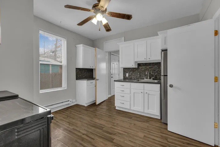 Kitchen featuring wood-finish flooring, white cabinetry, dark countertops, a mosaic tile backsplash, and a stainless steel refrigerator