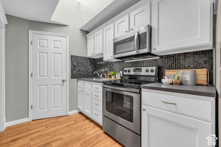 Kitchen featuring white cabinetry, stainless steel appliances, dark mosaic tile backsplash, and wood-finish flooring