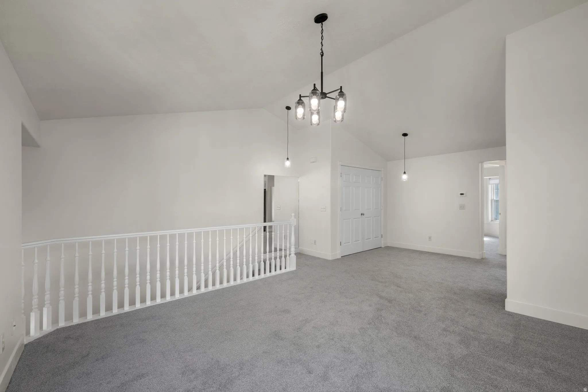 Vaulted ceiling, contemporary chandelier, crisp white walls, light gray carpeting, and white baluster railing