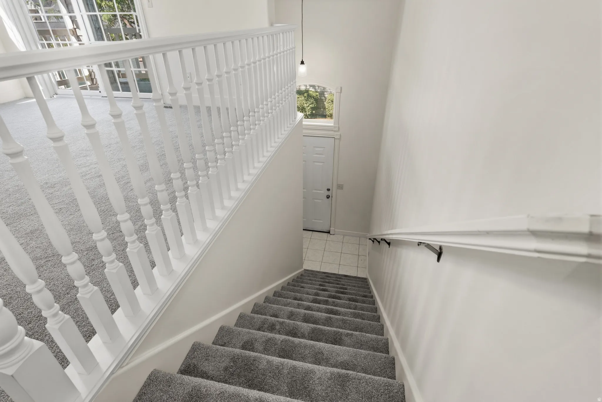 Carpeted staircase with white balusters and handrail, leading to a tiled entry with a white door and transom window