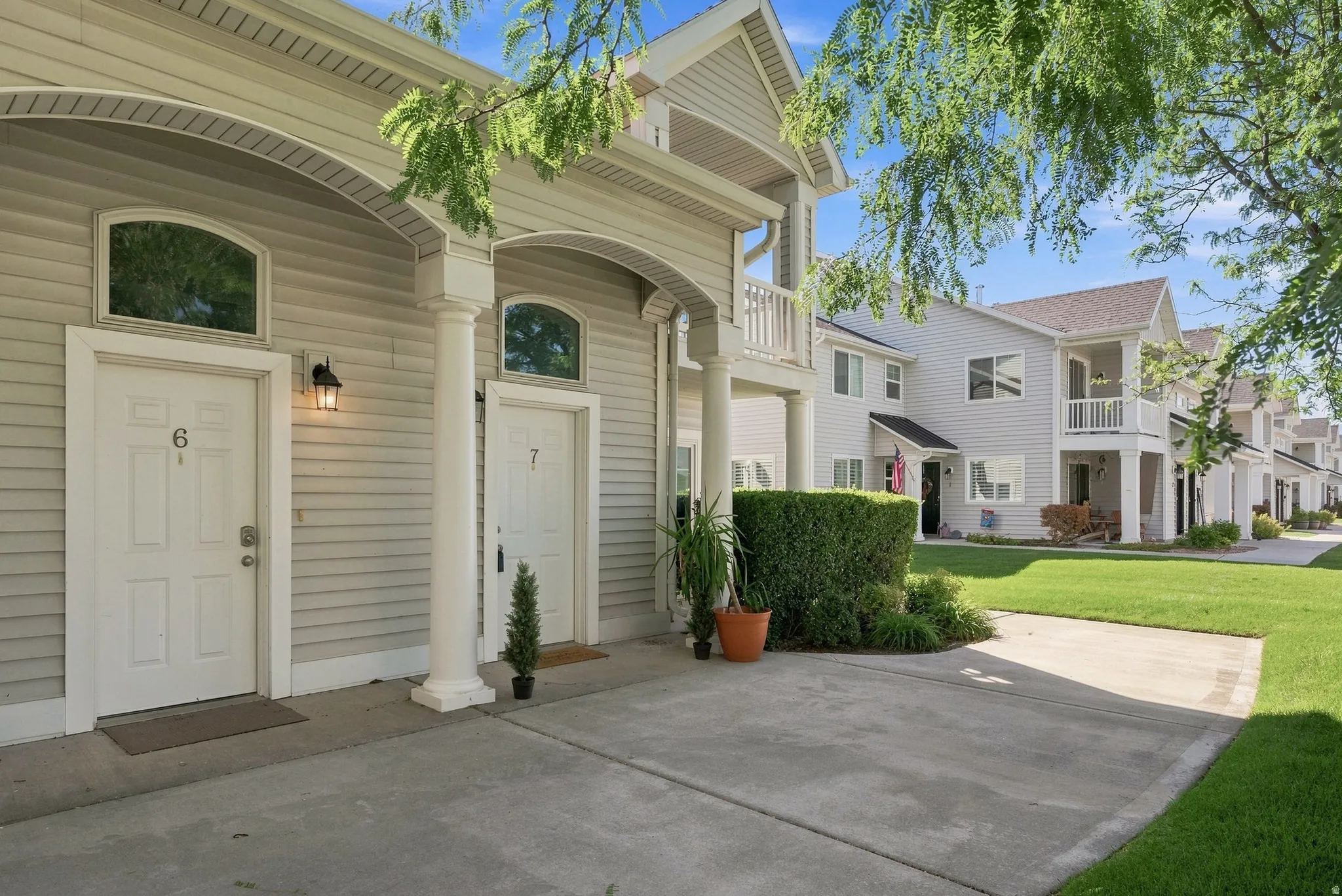 Light-colored siding exterior, arched portico entrances, column accents, upper-level balconies, and manicured green spaces