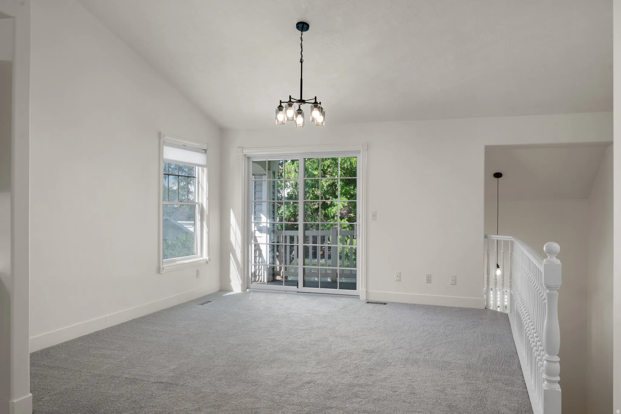 Vaulted ceiling with an industrial-style chandelier, light gray carpeting, and white painted walls