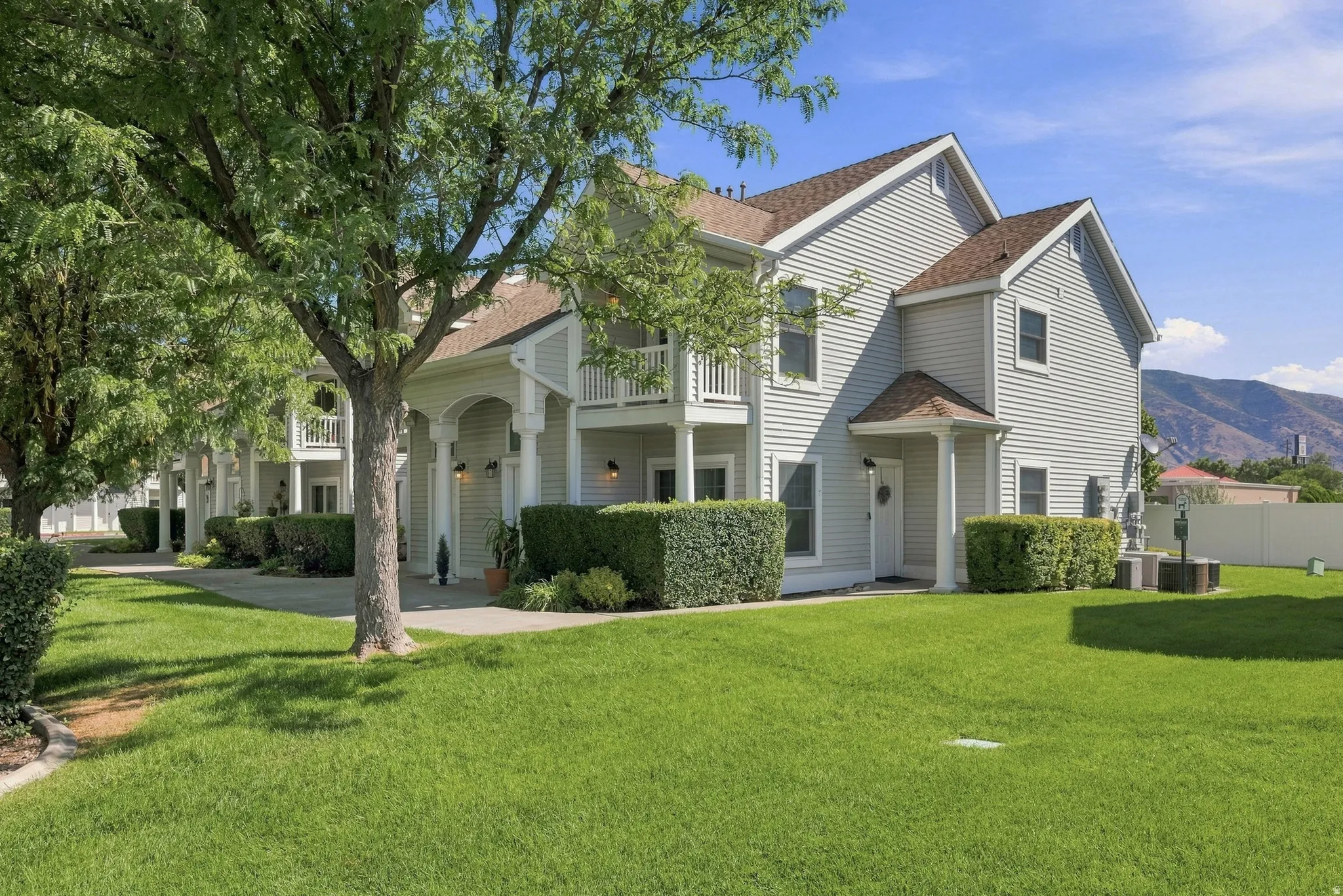 Building exterior with light gray siding, brown shingle roofing, white trim, and a white balcony