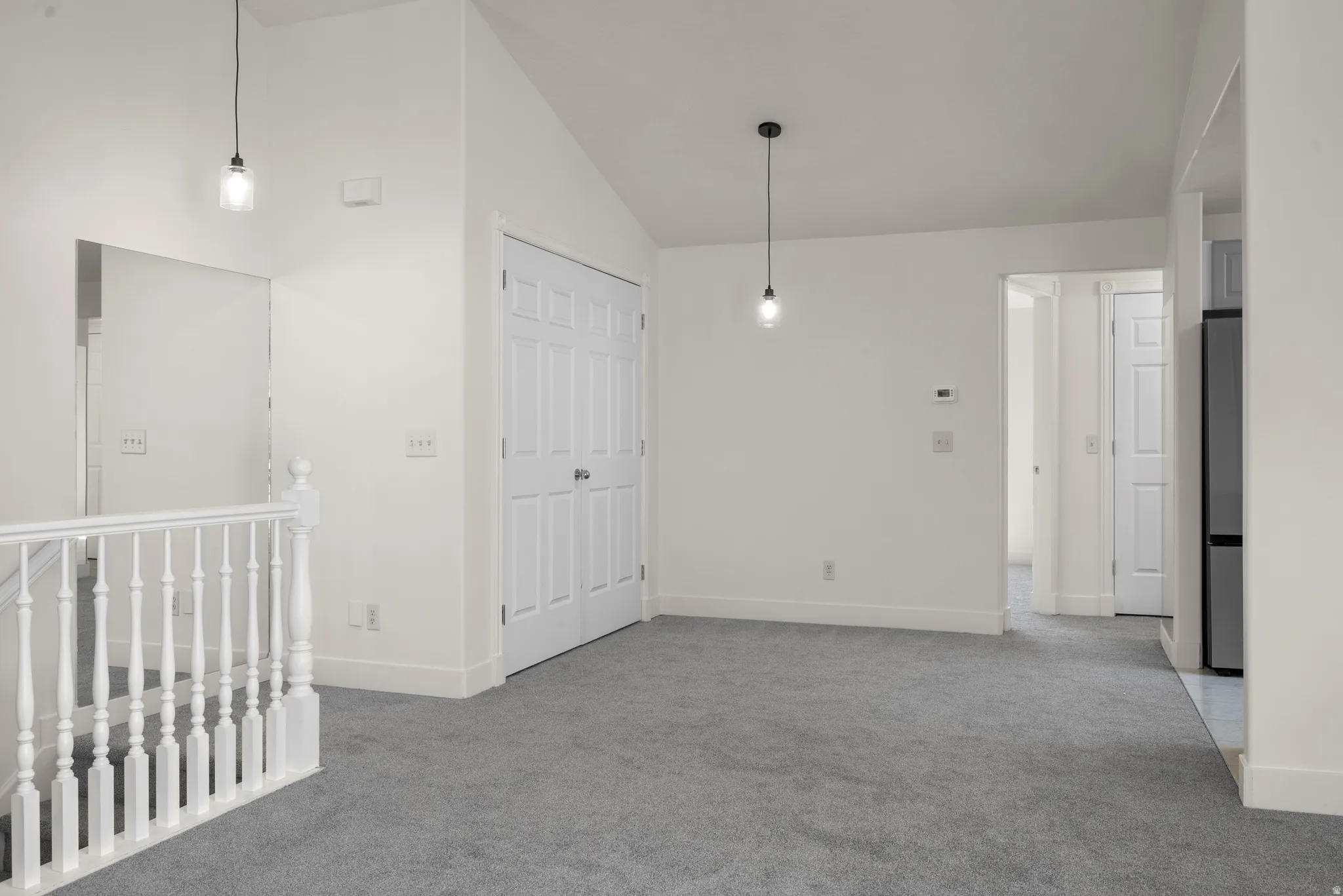 Vaulted ceilings, neutral gray carpet, white wall paint, classic white balusters, and contemporary pendant lighting