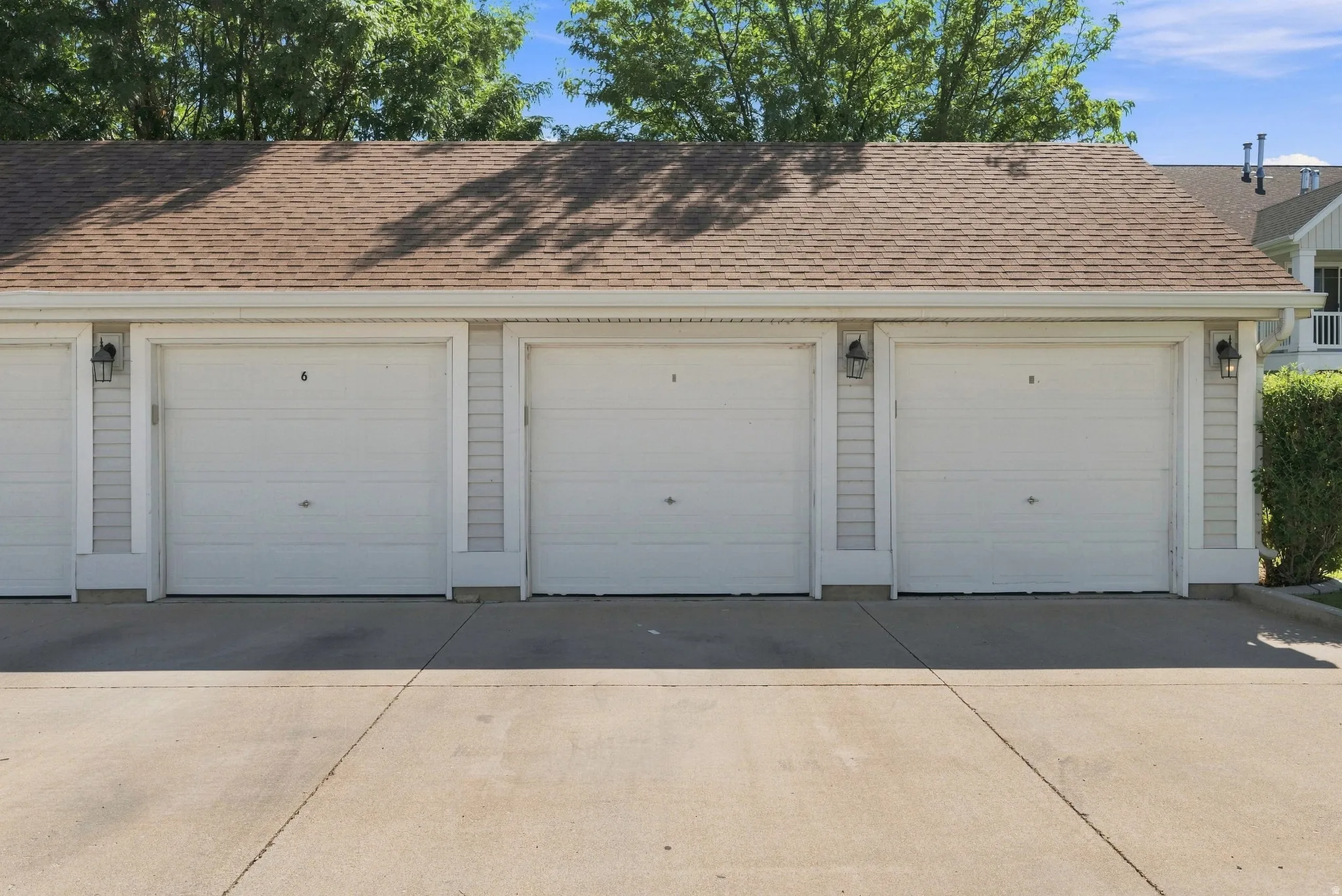 Individual garage doors with paneling, exterior lighting, light-colored siding, and a brown shingle roof