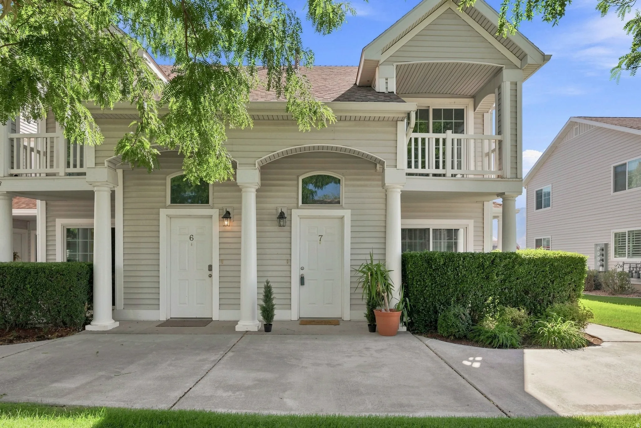 Light-colored siding exterior with a covered entry, upper-level balcony, arched window transoms, and columnar accents