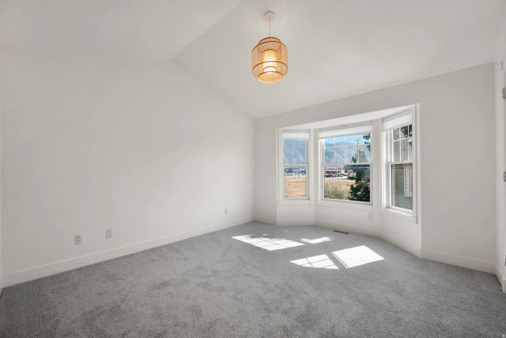 Vaulted ceiling, bay window, natural light, wall-to-wall carpeting, and a drum pendant light fixture