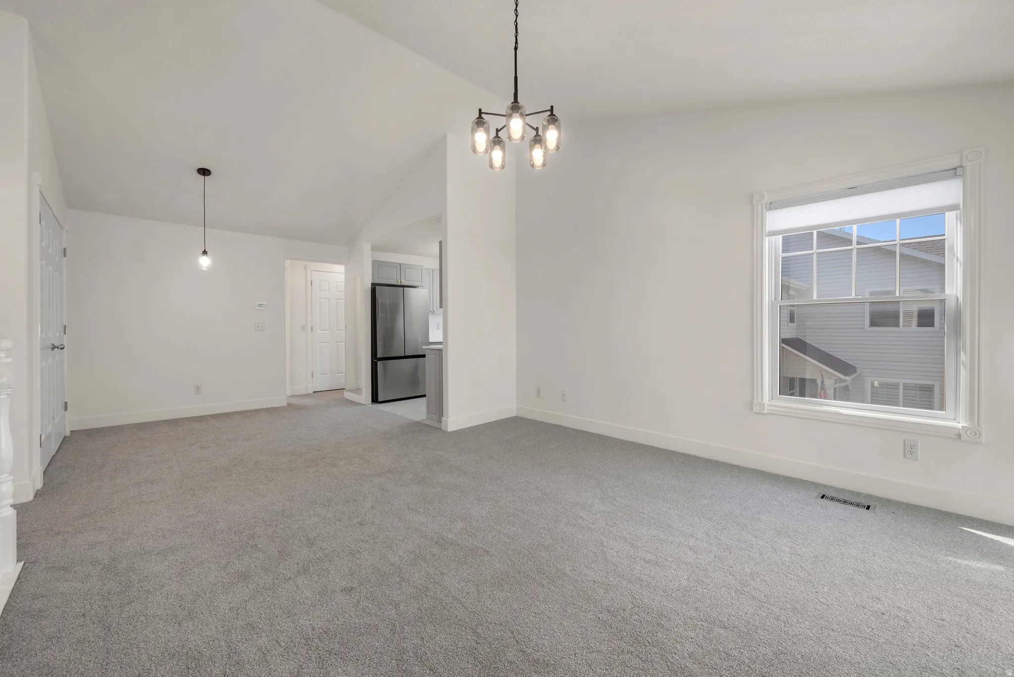 Carpeted living area with white walls, a large window, a modern chandelier, and an additional pendant light