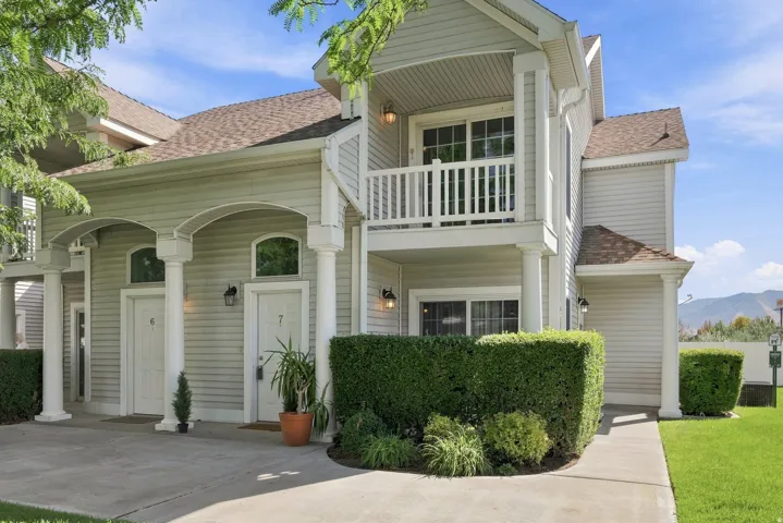 Siding exterior with architectural columns, arched entryways, upper-level balcony, paved walkway, and manicured hedges