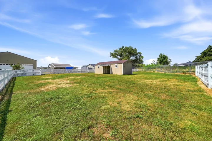 Expansive outdoor area featuring a wooden shed structure, white fence perimeter, and established trees