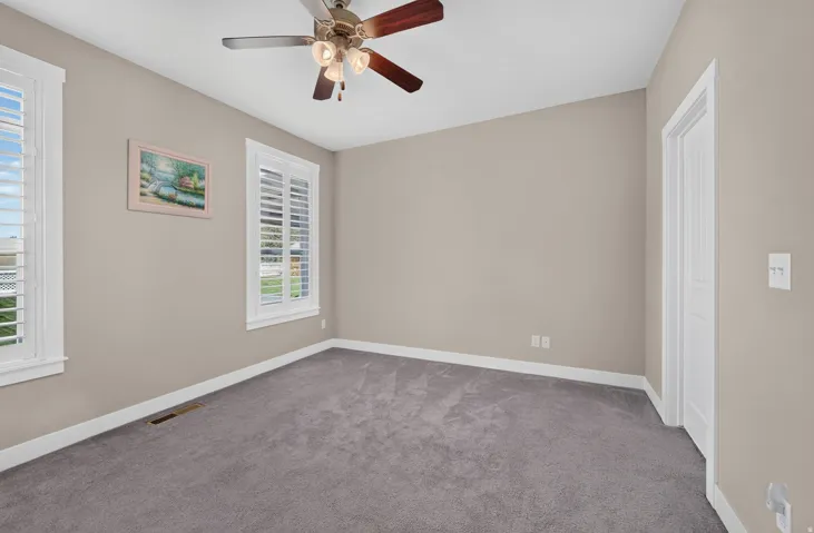 Neutral wall paint, gray carpeting, a ceiling fan with integrated lighting, and white window shutters