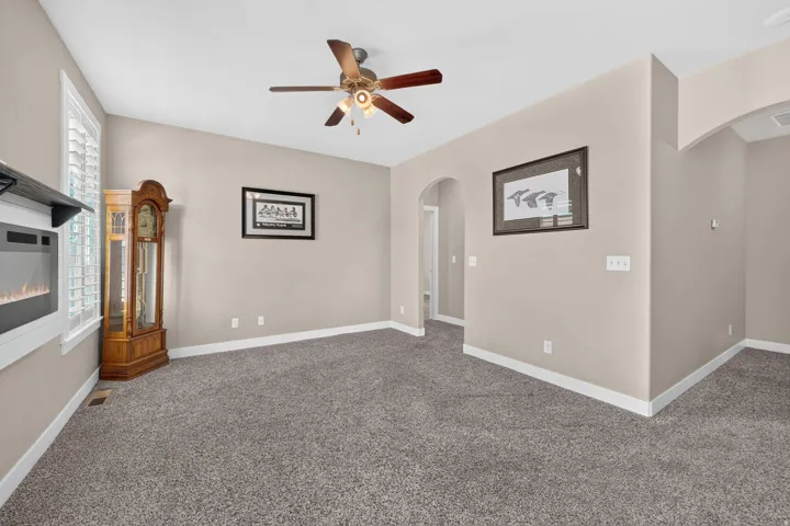 Recessed wall-mounted fireplace, window with plantation shutters, ceiling fan with light fixture, arched doorway, and neutral-toned wall paint
