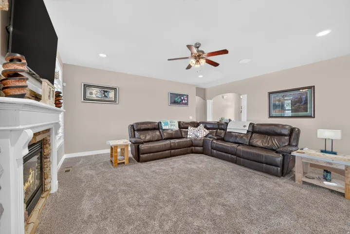 Built-in fireplace with stone surround and white mantel, recessed lighting, and ceiling fan