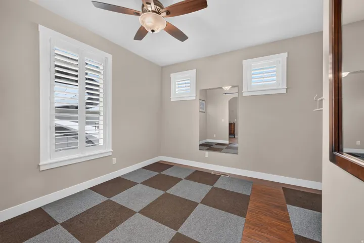 Ceiling fan, wood-finish flooring, checkerboard carpet, three windows with white plantation shutters, and a wall alcove