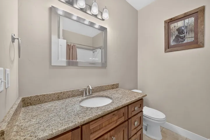 Wood-finish vanity with polished hardware, granite countertop, undermount sink, and wall-mounted vanity lighting