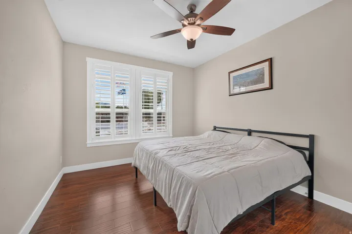 Wood-finish flooring, dual windows with plantation shutters, and a ceiling fan with integrated lighting