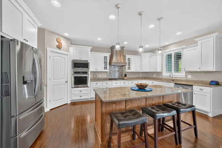 Expansive kitchen featuring wood-finish flooring, white cabinetry, stainless steel appliances, a center island with a granite countertop, and recessed lighting