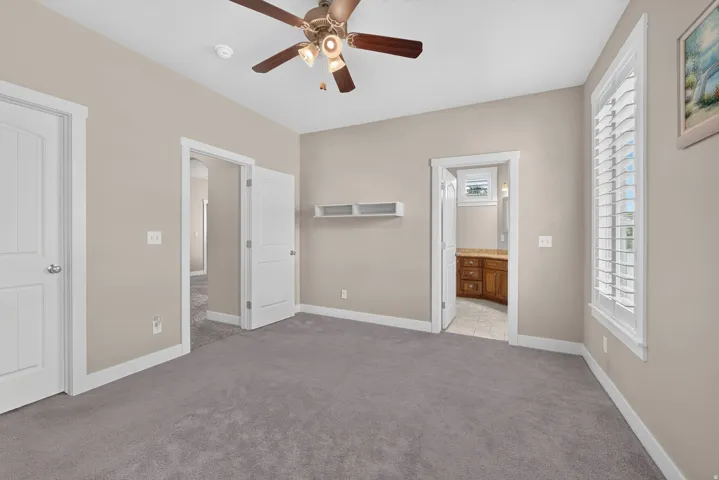 Vaulted ceiling with a ceiling fan, neutral wall paint, gray carpeting, white louvered window shutters, and white trim