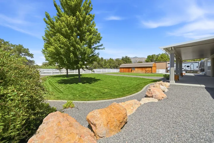 Expansive gravel hardscaping with large boulder accents, covered patio, manicured lawn, and mature trees