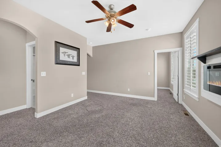 Integrated electric fireplace, ceiling fan with light fixture, carpeted flooring, and white window shutters