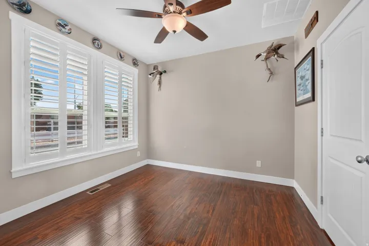 Wood-finish flooring, plantation shutters, ceiling fan with integrated lighting, white trim, and a paneled door