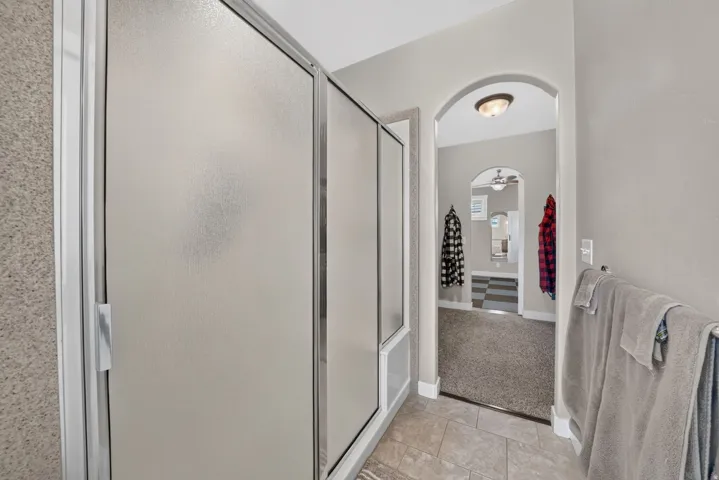 Frosted glass shower enclosure, tiled bathroom flooring, archway, and wall-mounted light fixture