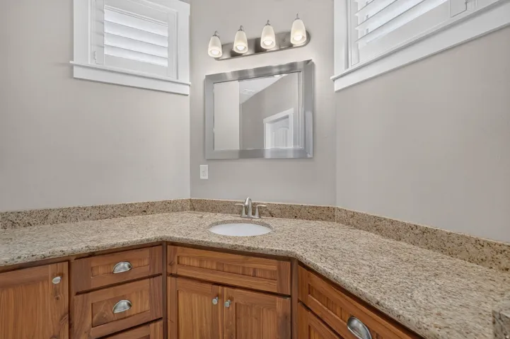U-shaped vanity with wood cabinetry, light-toned granite countertop, undermount sink, and wall-mounted light fixture