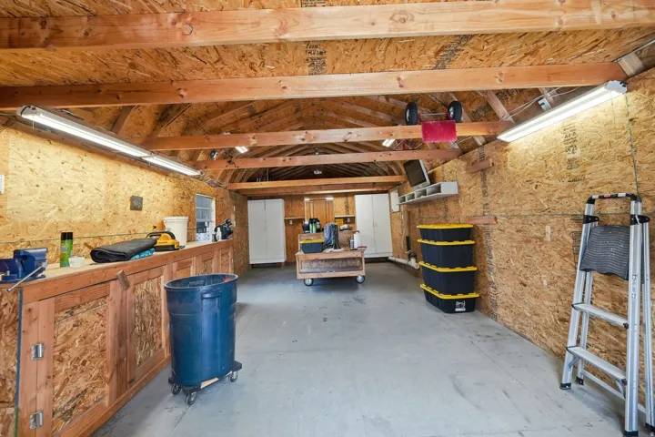 Exposed wood beam ceiling with fluorescent lighting, built-in workbench, and concrete flooring