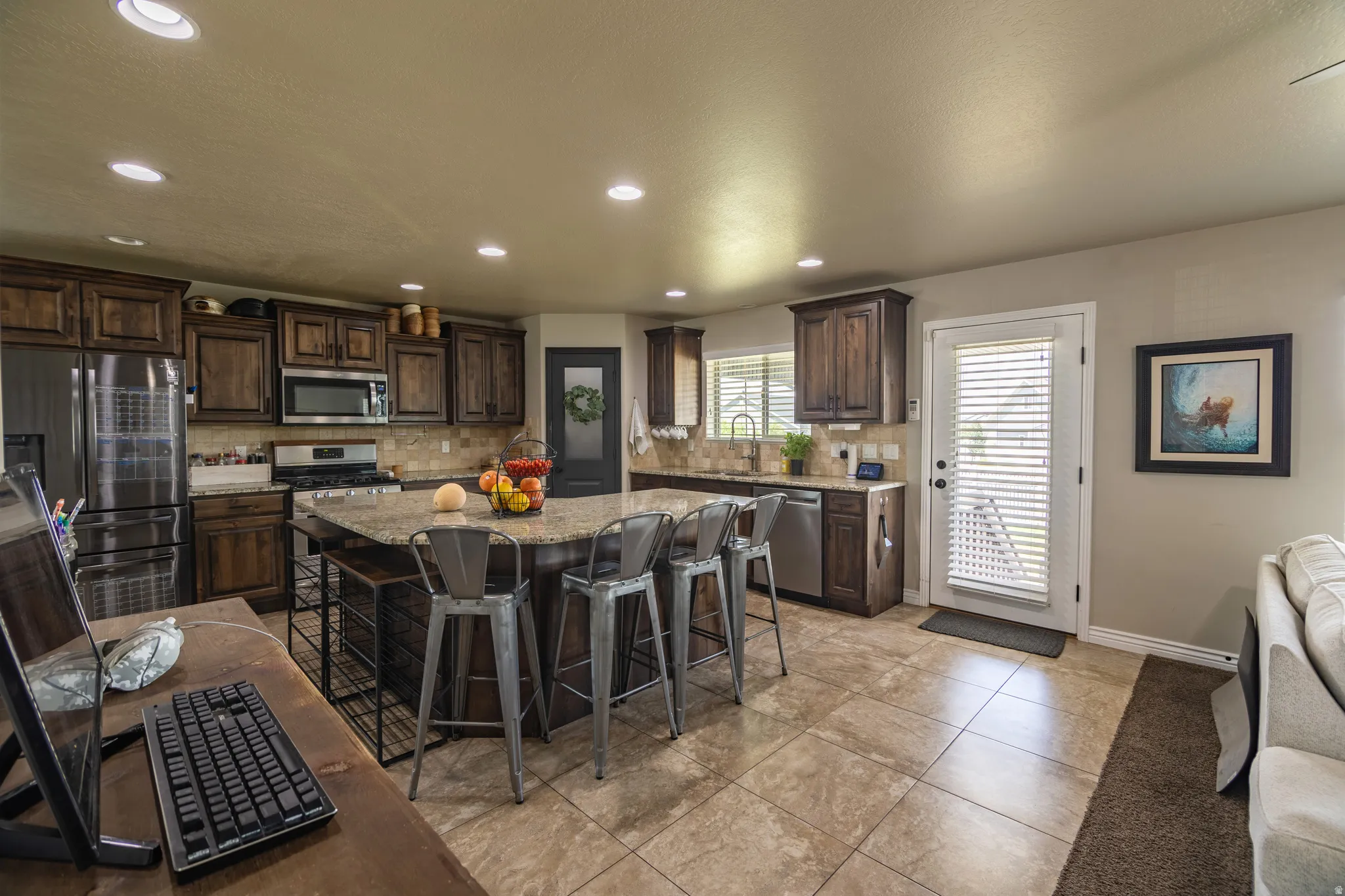 Spacious kitchen featuring an expansive center island with seating, stainless steel appliances, dark wood cabinetry, and recessed lighting